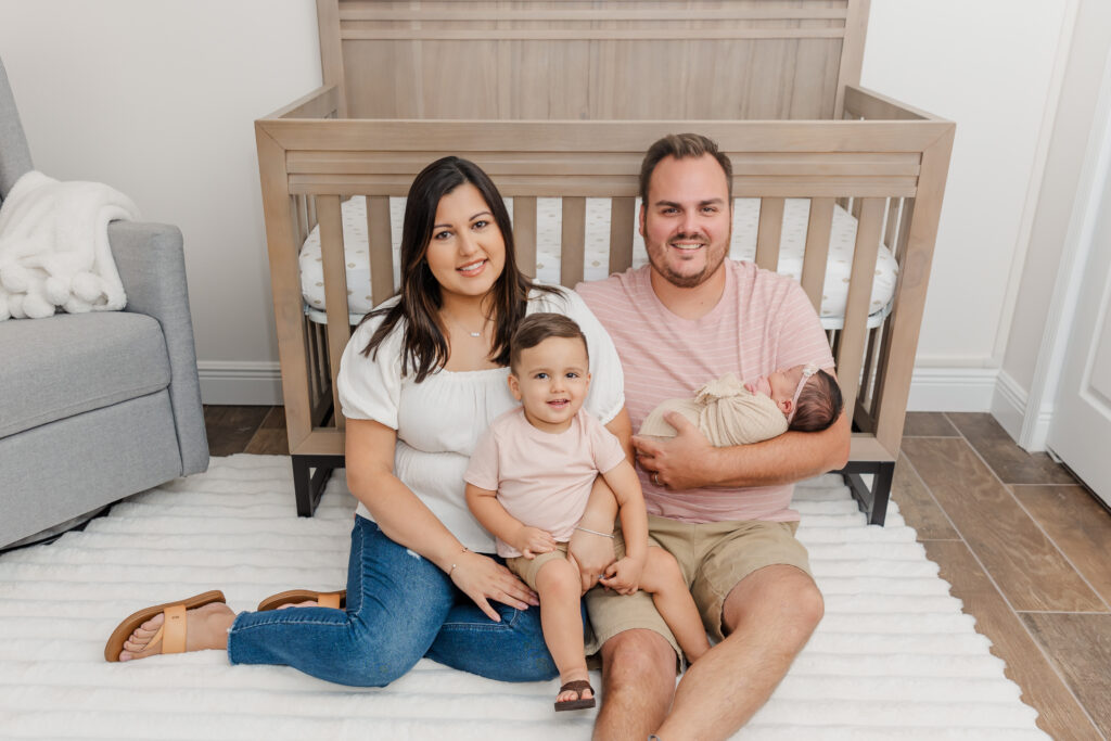 family cuddled on floor in front of crib in nursery during lifestyle newborn photo session