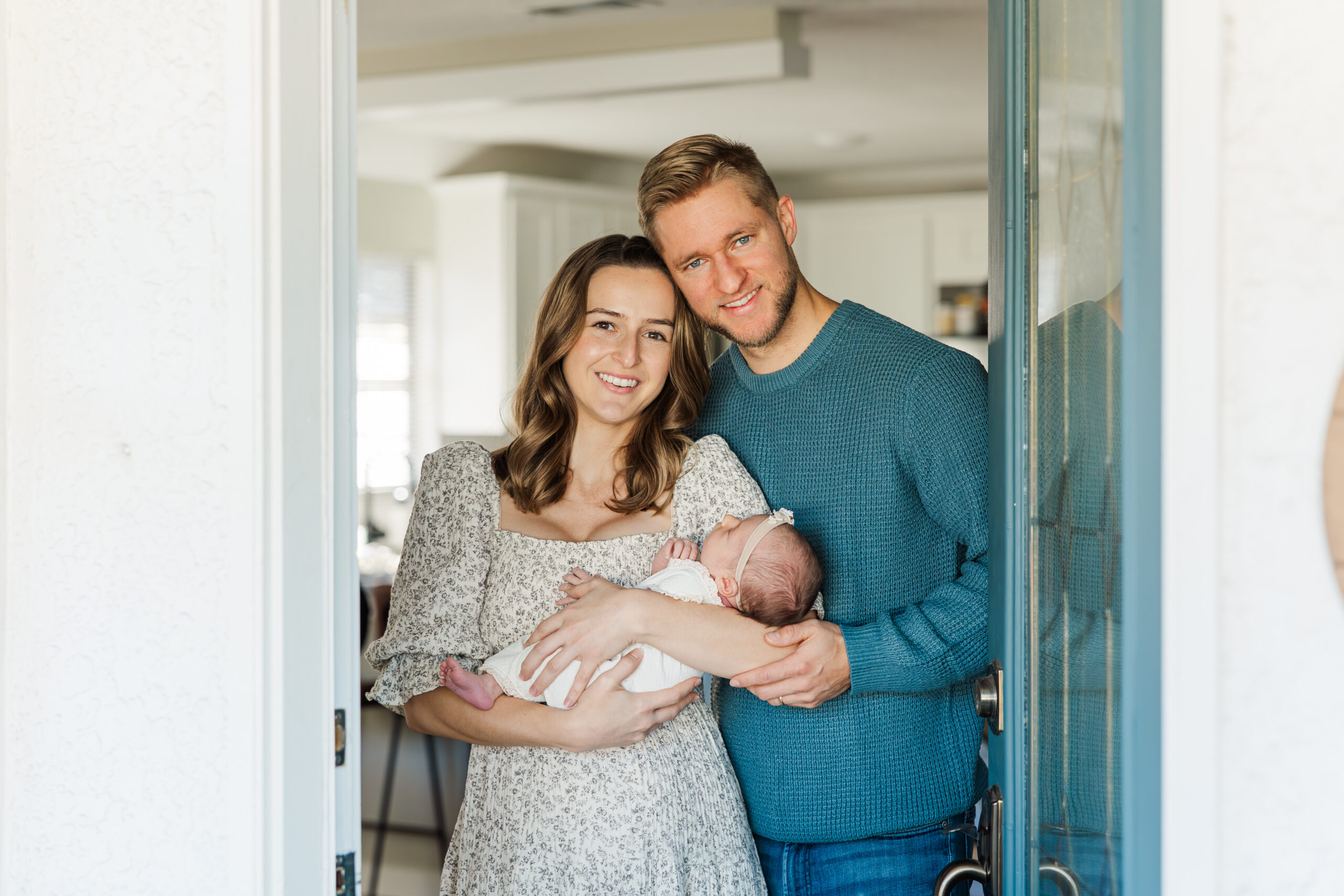 Mom and dad cradling baby standing in their doorway at home for lifestyle newborn session